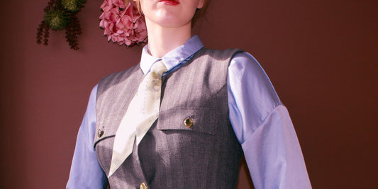 Person wearing a gray vest over a light blue shirt with the soft floral mint green Morning Reverie silk twilly scarf by The Line Atelier