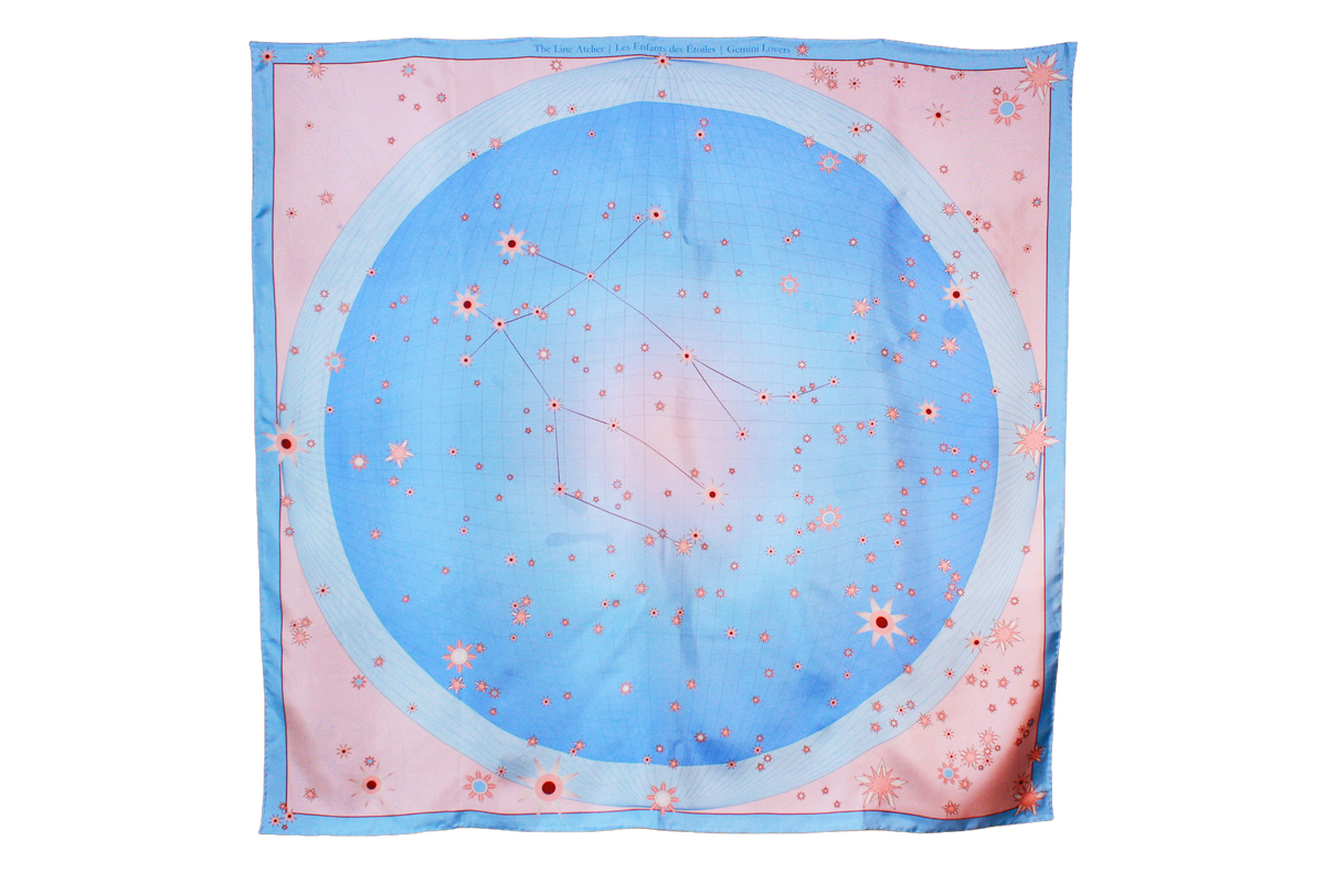 A square silk scarf featuring a celestial design of the Gemini constellation with a large light blue circle, constellation lines, and small stars on a soft pink background, finished with a light blue border and line art of ballet dancers in pairs.