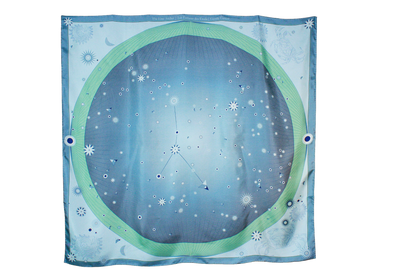 A square scarf featuring a celestial design with a light blue starry sky, a green ring, and the Cancer constellation patterns, hanging on a brown wall.