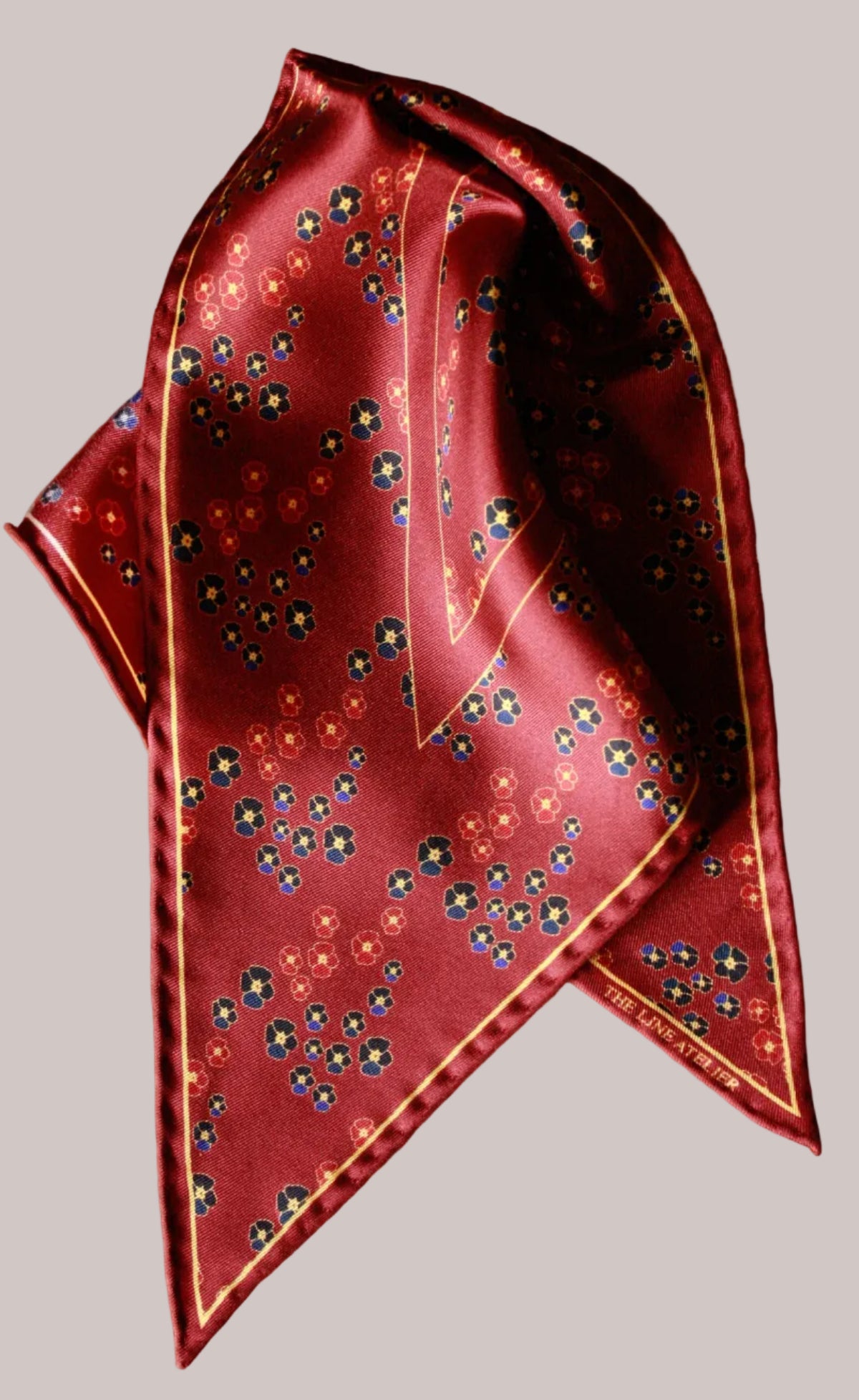 Folded red silk diamond scarf with floral pattern on a beige background