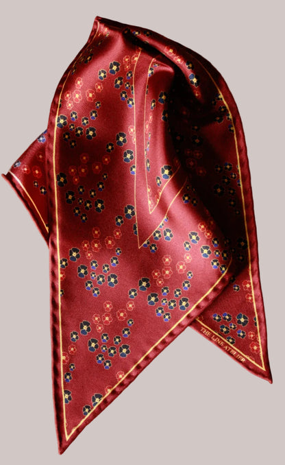 Folded red silk diamond scarf with floral pattern on a beige background