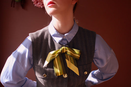 Model wearing Autumn Sage green silk twilly scarf by The Line Atelier in a bow paired with a vest and blue blouse