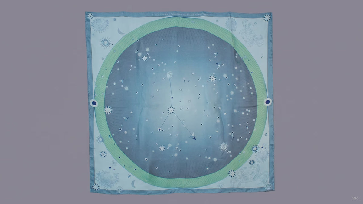 A square scarf featuring a celestial design with a light blue starry sky, a green ring, and the Cancer constellation patterns, hanging on a brown wall.